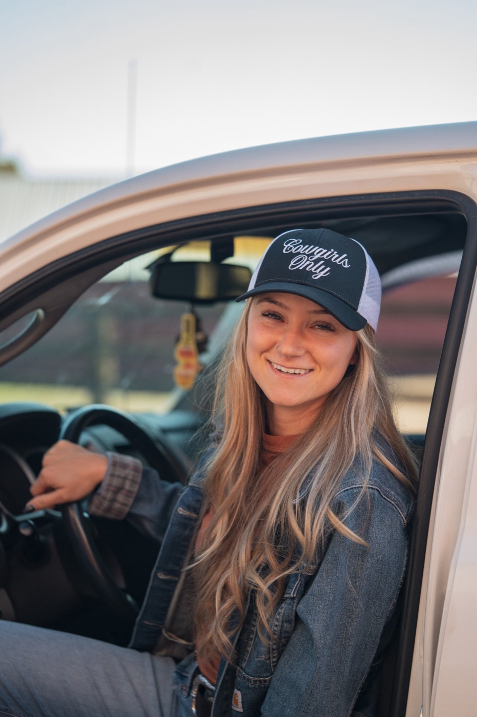 Smiling model in a Cowgirls Only cap at the wheel of a truck