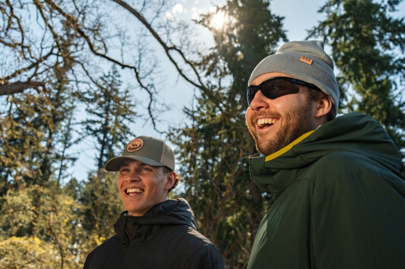 Two friends smiling in the sun under evergreen trees