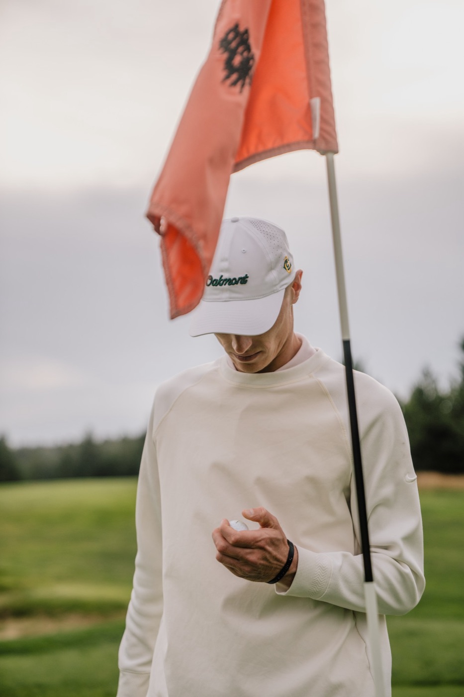 Golfer in a white Oakmont cap holding a ball beneath an orange flag