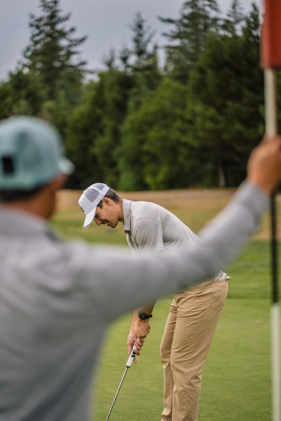 Golfer lining up a putt while a friend holds the flag