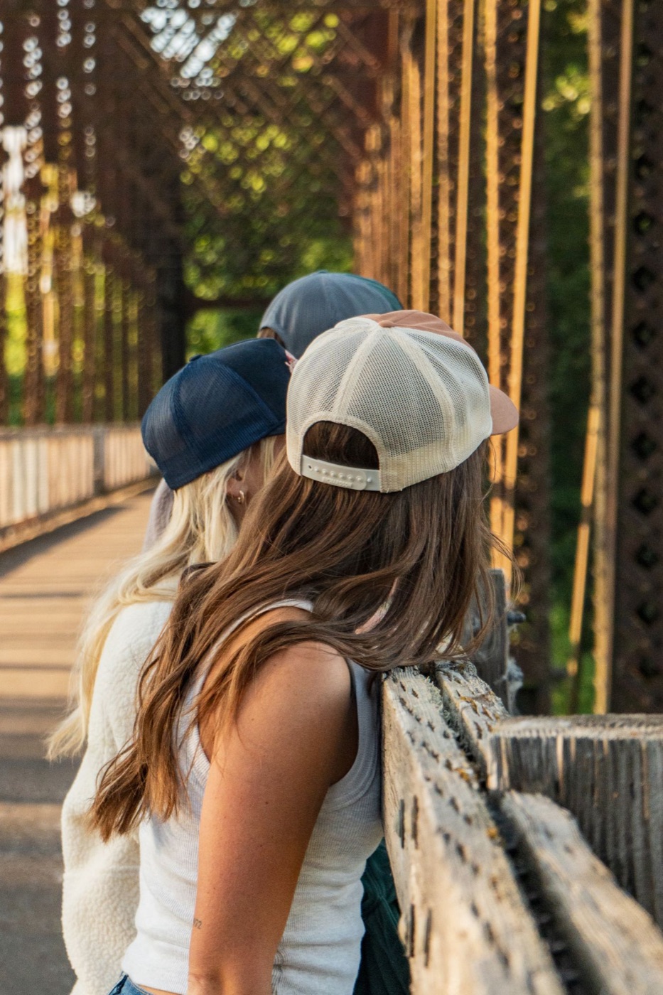 Friends in trucker caps leaning on the bridge railing, seen from behind