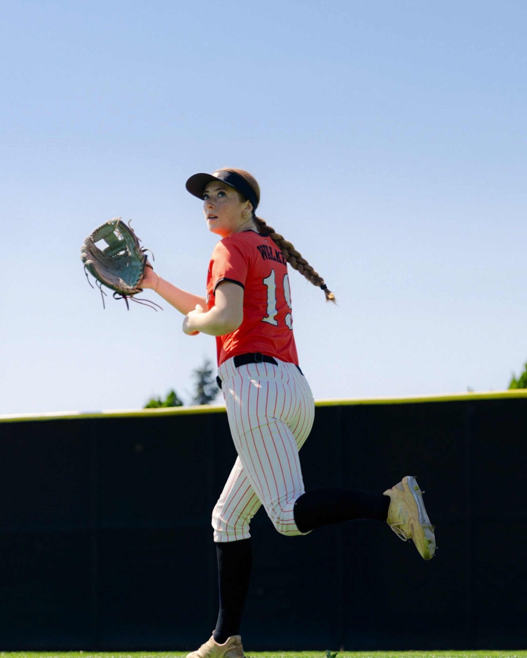 Softball player in a red jersey running with her glove