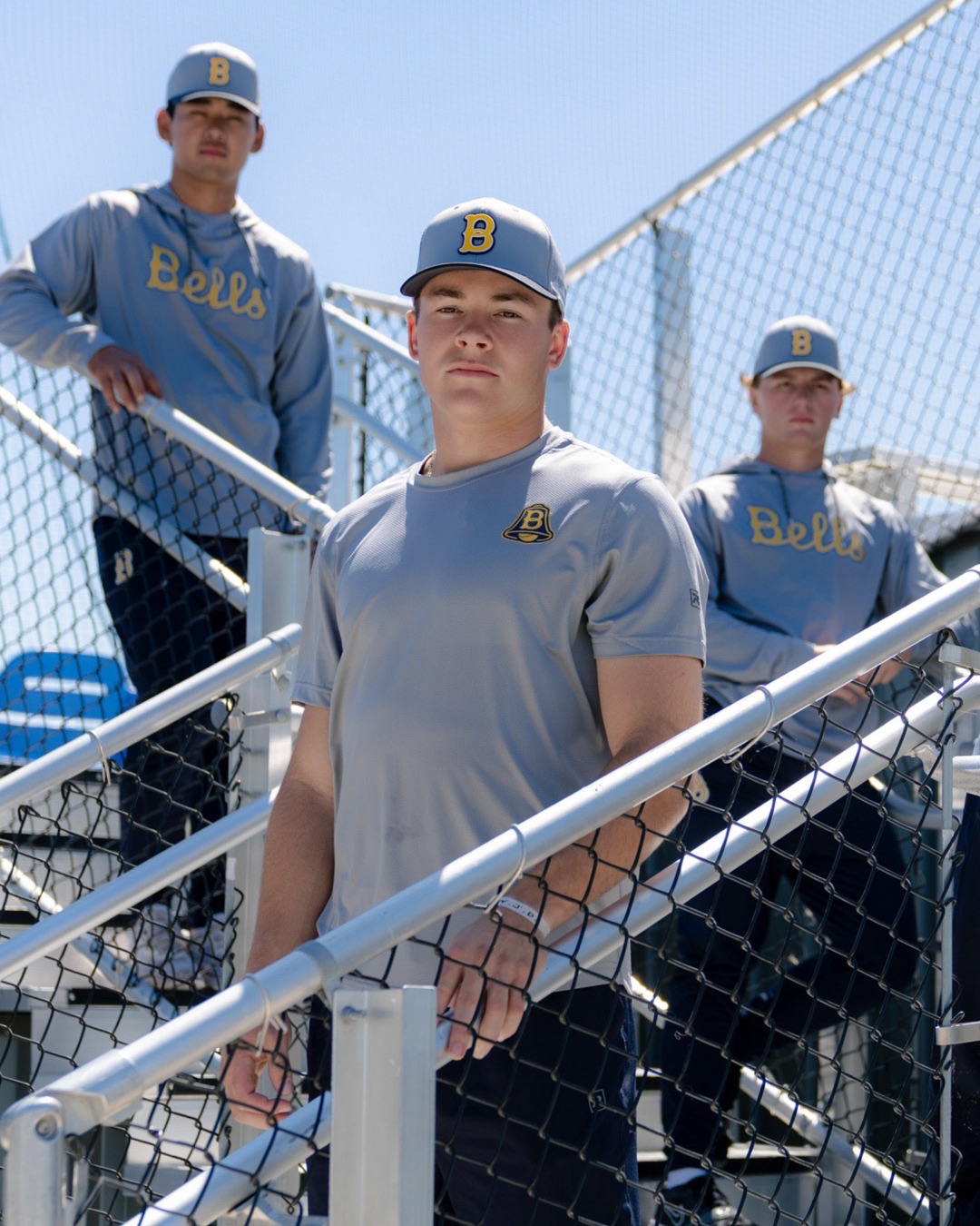 Players in gray Bells shirts standing in the dugout