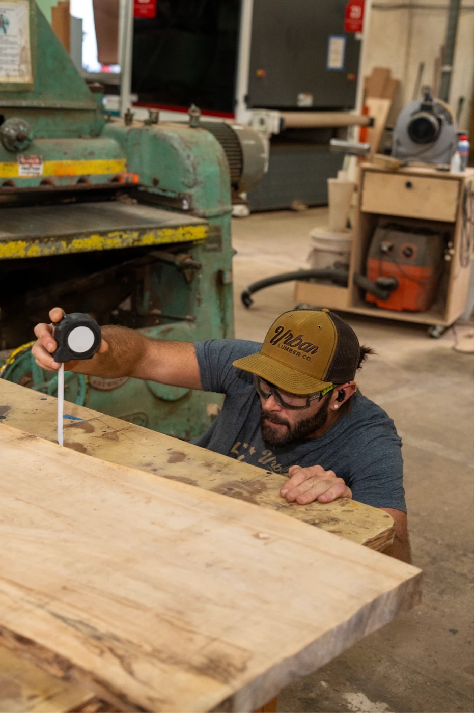 Woodworker in an Urban Lumber cap measuring a live-edge slab