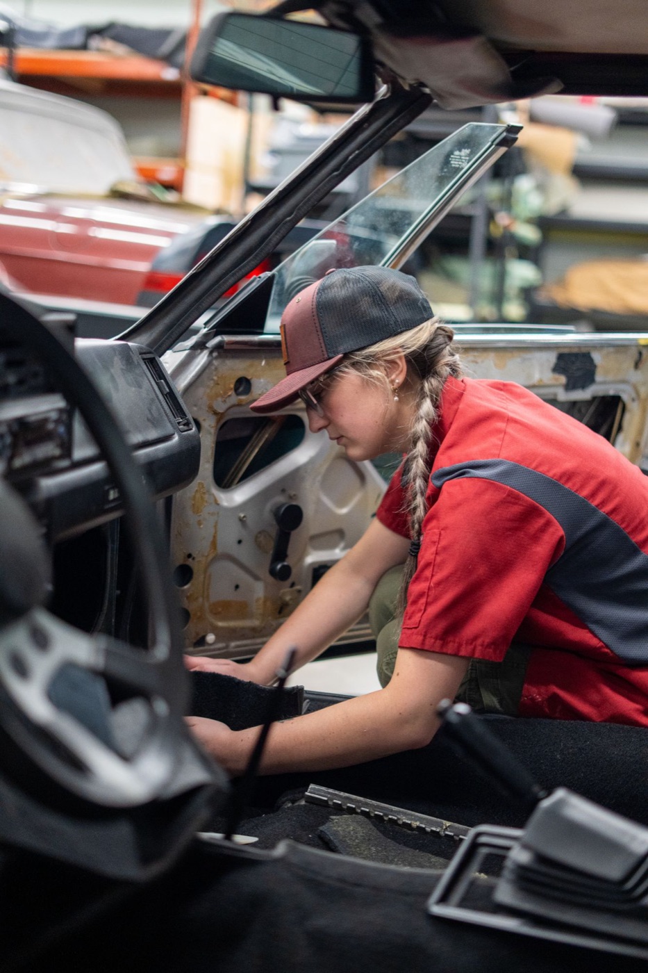 Mechanic in a maroon trucker working inside a classic car